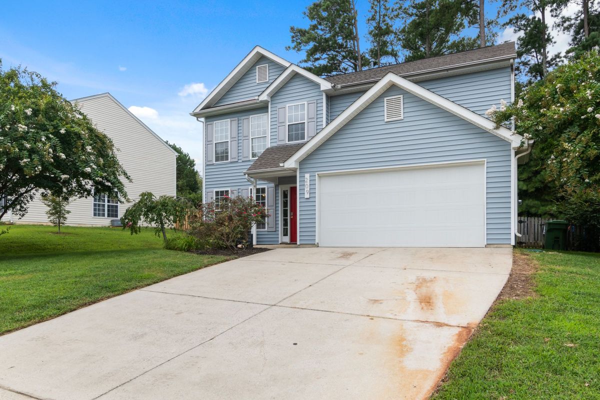 A pale blue home with a large white garage door among mature trees