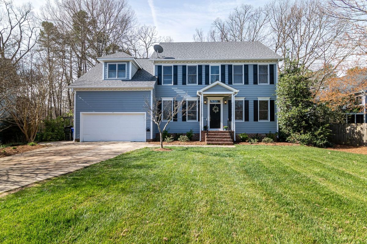 A blue two-storey home among tall trees with an attached single garage door