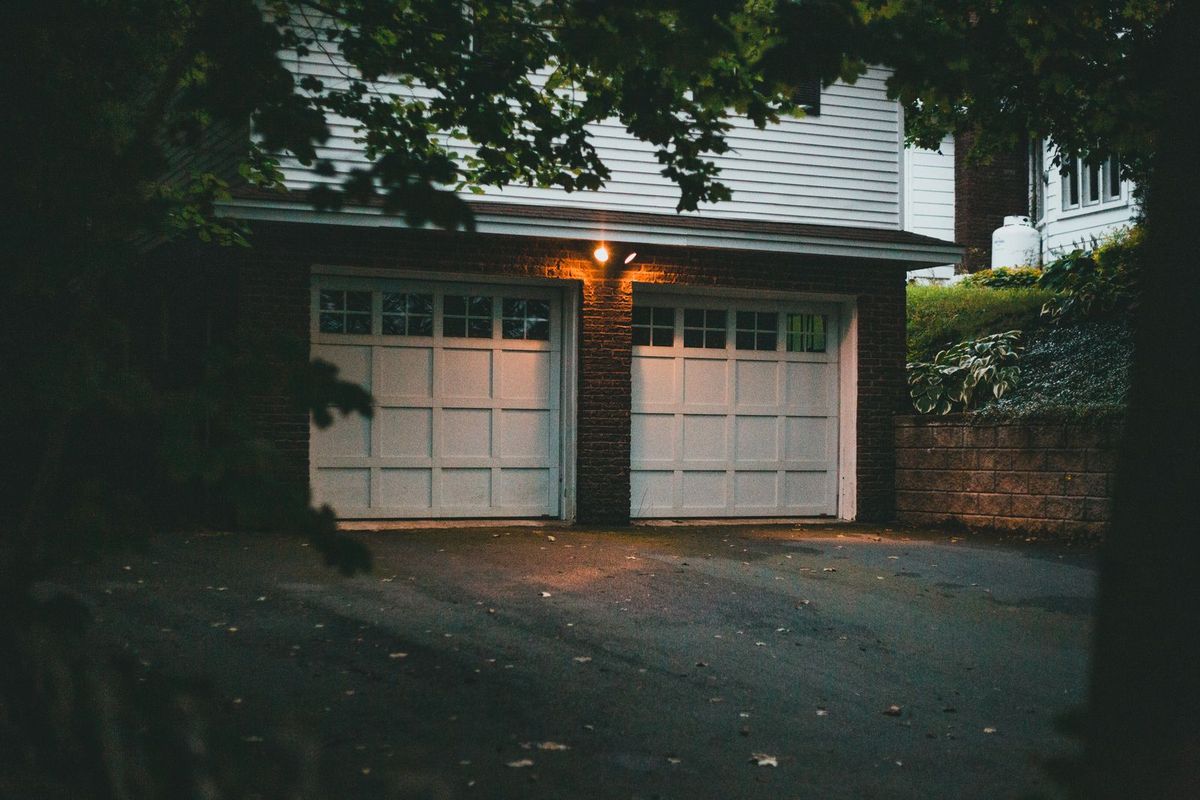 A double carriage-style garage door with window panels lit by a porch light at night