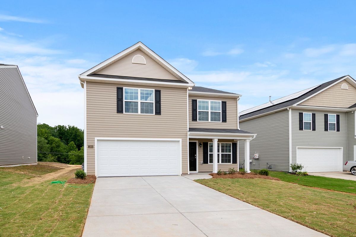 A beige two-storey home with a white double garage door and a young lawn